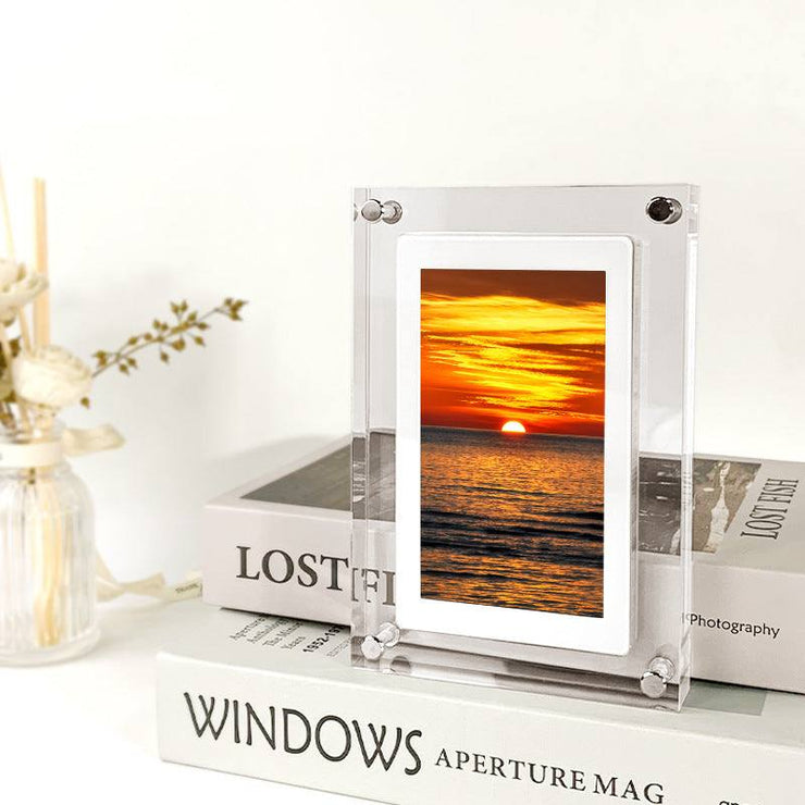 Digital picture frame with acrylic design displaying a sunset, placed on books.
