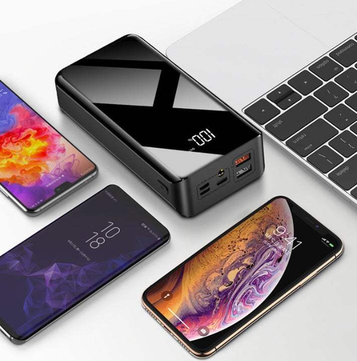 30000mAh power bank with LCD display charging multiple devices near laptop.