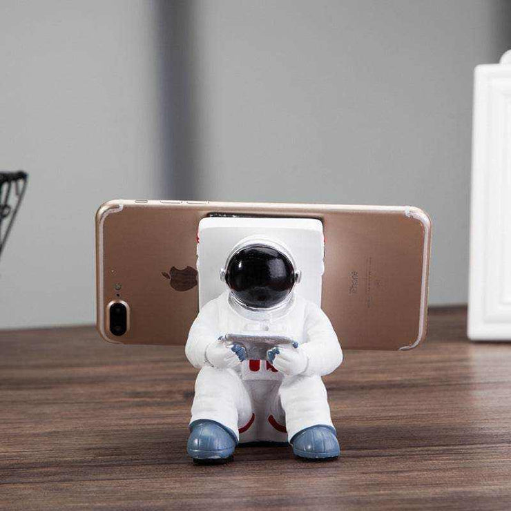 Astronaut-shaped phone stand holding a smartphone on a wooden desk.