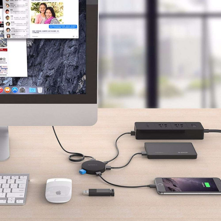 ORICO HA4U-U3 USB3.0 hub on desk with charging devices and computer setup.