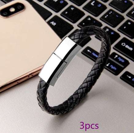 Black braided leather bracelet USB charger next to smartphone and laptop keyboard.