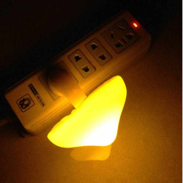 LED night light in mushroom shape plugged into wall socket, emitting warm yellow glow.