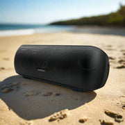 Subwoofer Bluetooth Speaker on sandy beach with ocean background.