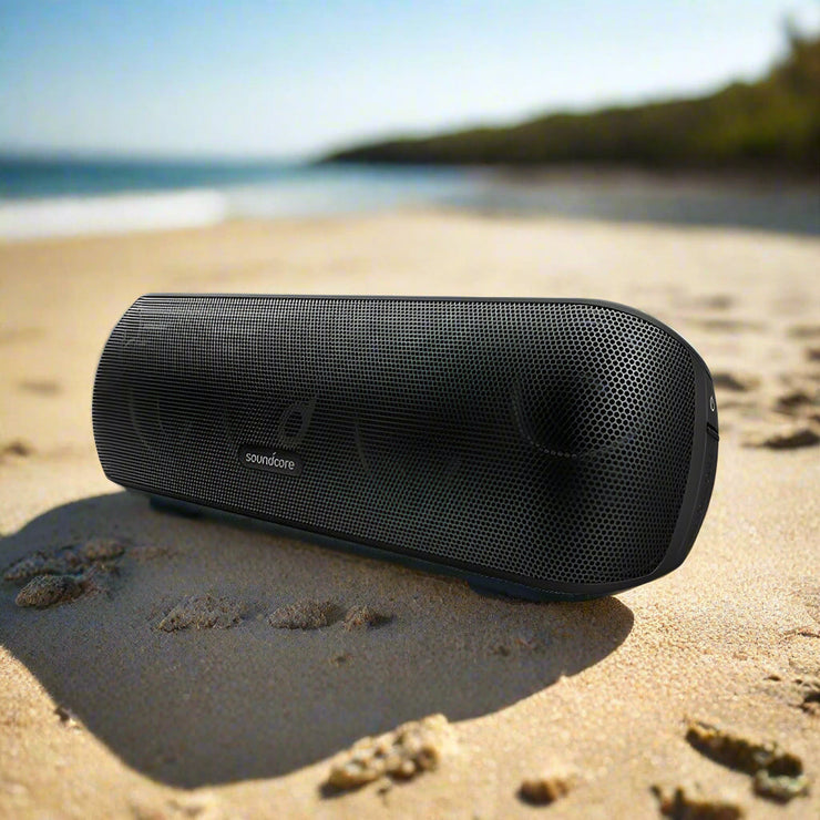 Subwoofer Bluetooth Speaker on sandy beach with ocean background.