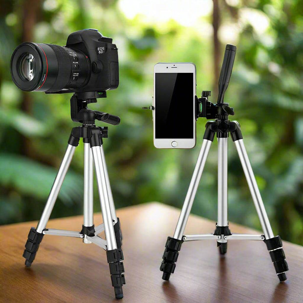 Professional camera tripod stand with phone holder, silver and black, on a wooden table, outdoor background.