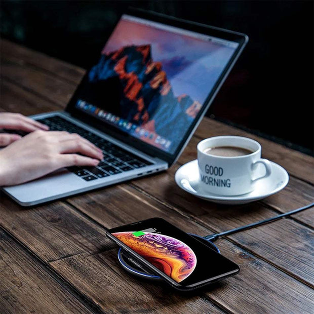 Wireless charger on desk with charging smartphone next to a laptop.